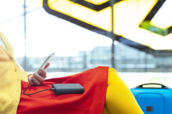 O persoană stă în sala de așteptare a unui aeroport și își încarcă smartphone-ul cu un Hama power bank.