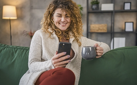 O femeie stă pe o canapea verde confortabilă și își folosește smartphone-ul pentru a-și controla casa inteligentă.