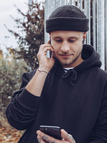 Young man wearing the Hama "Spirit Pocket" Bluetooth headphones and operating his cell phone