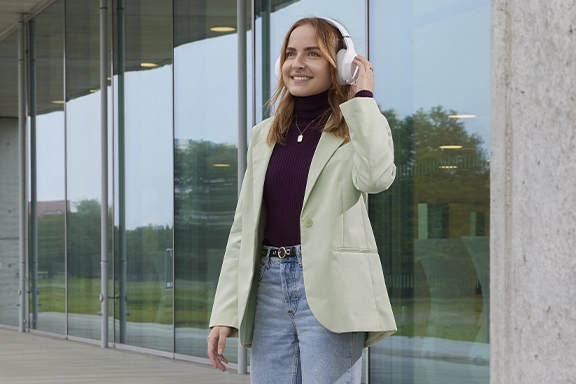 A young woman steps down the stone steps in front of a building wearing Hama Bluetooth® headphones "Spirit Calypso II"