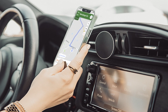 Inside a car, a hand attaches a smartphone to the Hama "MagLock" car mobile phone holder, which is installed on the air vents.