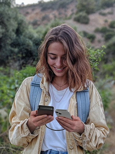 A young woman is hiking in the countryside and uses her smartphone while charging it with the Hama Power Pack "PD 20"